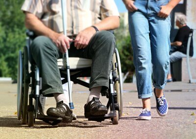 Une jeune femme accompagne une personne en fauteuil roulant en promenade.
