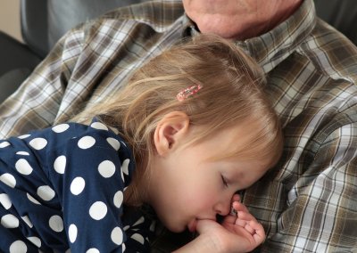 Une petite fille fait la sieste sur le torse d'un monsieur âgé.
